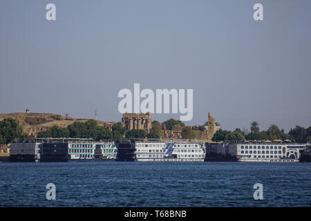 Kom Ombo, Egitto: navi da crociera allineati lungo la riva del fiume Nilo; Il Kom Ombo tempio in background. Foto Stock