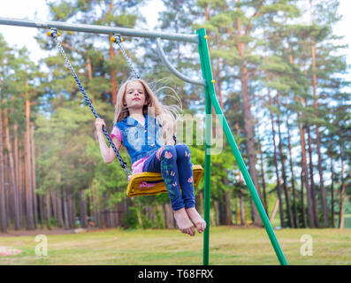 Bella ragazza bionda oscillare all'aperto sul parco giochi Foto Stock