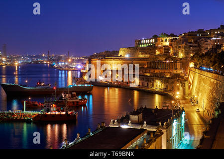 La vista notturna di Grand Harbour con il carico delle navi ormeggiate vicino a Santa Barbara bastione, La Valletta. Foto Stock