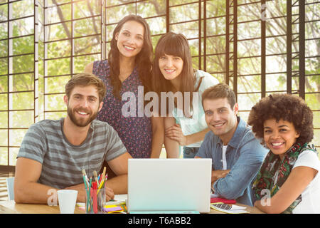 Immagine composita di felice creativo team di business riuniti attorno a un computer portatile Foto Stock