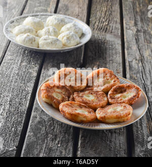 Tradizionalmente, Russo materie e frittelle fritte con ricotta. La cheesecake su un di legno tavolo rustico. Il processo di cottura. Foto Stock