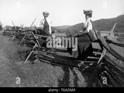 Due era vittoriana le donne passano il tempo seduti su una staccionata, ca. 1900. Foto Stock