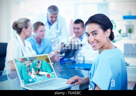 Immagine composita della bella sorridente medico digitando sulla tastiera con il suo team dietro Foto Stock