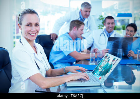 Immagine composita della bella sorridente medico digitando sulla tastiera con il suo team dietro Foto Stock