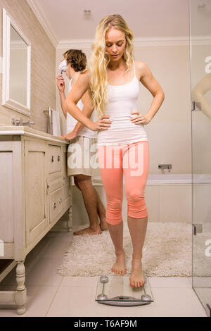 Donna bionda circa l'uso di una bilancia mentre il suo fidanzato la rasatura Foto Stock
