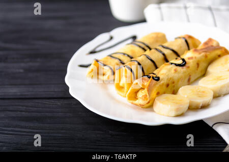 Frittelle di banane di sciroppo al cioccolato nero su sfondo di legno Foto Stock