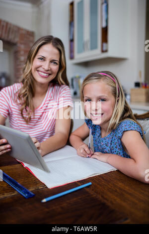 Madre utilizzando una tavoletta digitale mentre aiuta la figlia con i suoi compiti Foto Stock