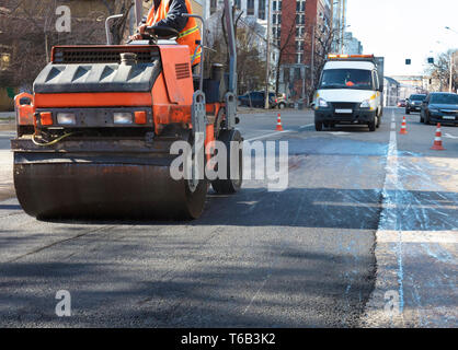 Pesante vibrazione compattatore a rulli riparazioni la strada sul manto di asfalto sul tratto stradale della carreggiata racchiuso da coni stradali Foto Stock