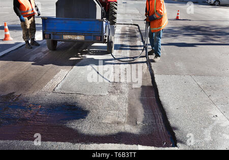 La manutenzione stradale lavoratore spruzza la miscela di bitume sull'area pulita per una migliore adesione al nuovo asfalto Foto Stock