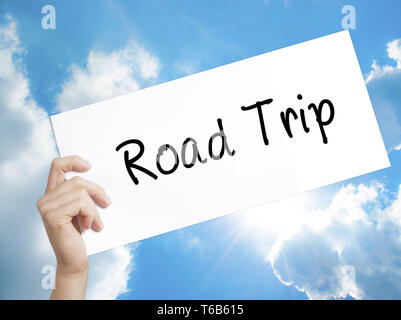 Viaggio su strada segno su carta bianca. Man mano che tiene la carta con testo. Isolato su sfondo cielo Foto Stock