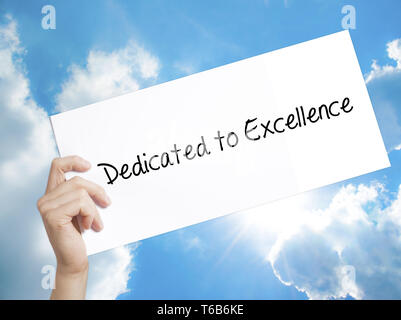 Dedicato all'eccellenza segno su carta bianca. Man mano che tiene la carta con testo. Isolato su sfondo cielo Foto Stock