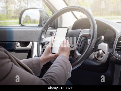 Femmina giovane conducente utilizzando il touch screen smartphone e la navigazione GPS in auto Foto Stock