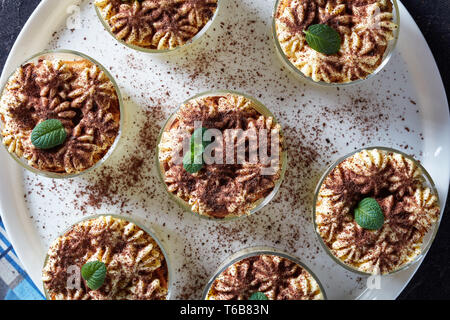 Classic tiramisù dolce italiano di biscotti savoiardi, uova, zucchero, caffè, mascarpone in bicchieri arrotondati su un piatto da portata, vista orizzontale da abo Foto Stock