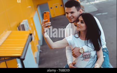 Giovane coppia adorabile che pongono insieme mentre rendendo selfie sullo smartphone su sfondo giallo Foto Stock