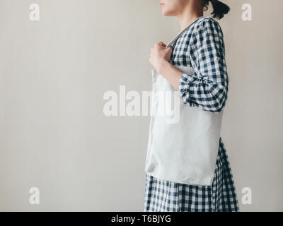 Blank tote bag modello di foto con spazio copia una giovane donna in un plaid abito di cotone è in possesso di un bianco riutilizzabili tote bag, sulla sua spalla Foto Stock
