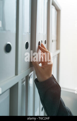 Imprenditrice navigando attraverso il ring binder file archivio di documentazione o il ripiano in ufficio business, stretta di mano Foto Stock