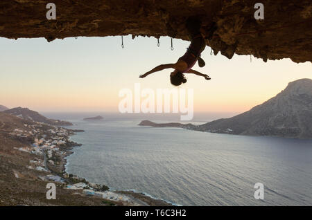 Female Rock scalatore appeso a testa in giù sul percorso impegnativo in grotta al tramonto, prima di appoggio mantenendo sul suo tentativo Foto Stock