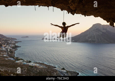 Giovani femmine rocciatore appeso sulla corda e stirando le armi. Rocciatore rilassante o ingannare intorno mentre viene abbassato contro picturesqu Foto Stock