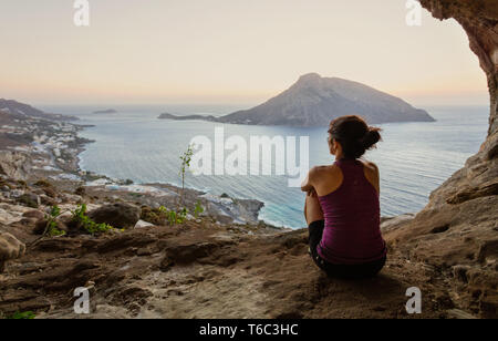 Femmina giovane scalatore seduta nella grotta e guardare il tramonto Foto Stock