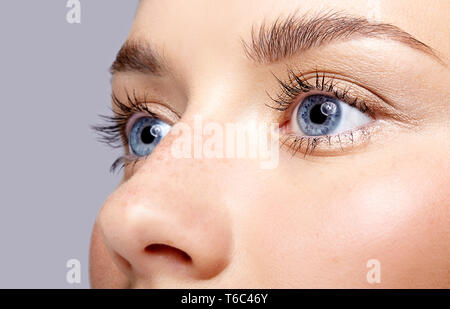 Macro Closeup ritratto di volto femminile. Donna Uomo aprire gli occhi blu con il giorno la bellezza del trucco. Ragazza con una pelle perfetta e lentiggini. Foto Stock