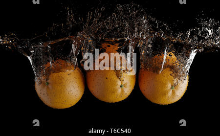 Gli spruzzi di frutta su acqua. Frutta fresca arancione essendo scattato come hanno sommerso sotto acqua su sfondo nero Foto Stock