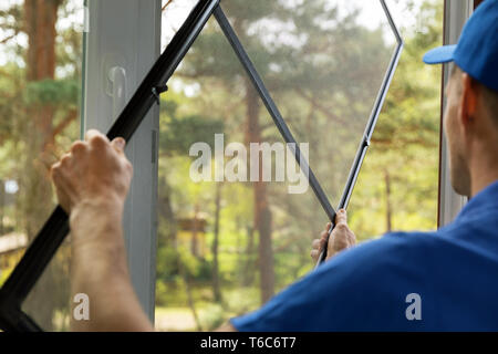 L'uomo installazione zanzariera wire mesh sulla finestra di casa Foto Stock