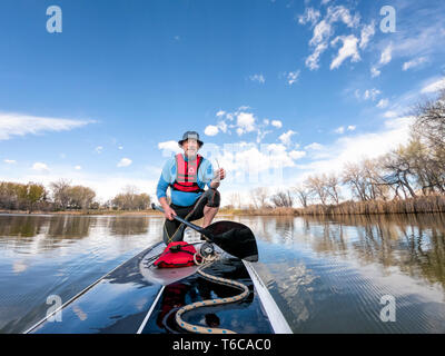 Senior atletico uomo su un stand up paddleboard su di un lago calmo in Colorado, vista di prua Foto Stock