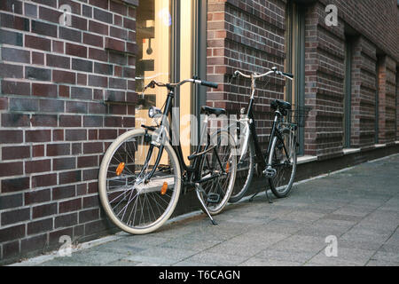 Le biciclette sono parcheggiato a fianco di un muro di mattoni di un edificio su una strada della citta'. Foto Stock