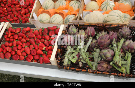 Stallo del fruttivendolo con scatole piene di frutta e verdure come le fragole i meloni e i carciofi Foto Stock