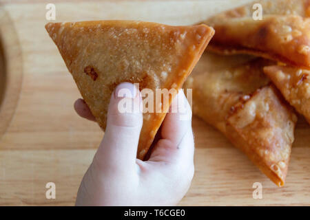 Una vista ravvicinata di un bambino tenendo un samosa nella loro mano pronto a mangiare Foto Stock