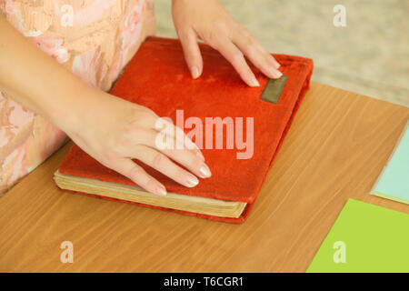 La donna mettere le mani sul coperchio rosso di un libro di foto o album, sulla scrivania. La vista dall'alto. Foto Stock