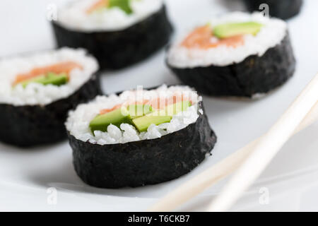 Rotoli di Sushi con salmone, avocado, riso nelle alghe marine e bastoncini su una piastra. Foto Stock