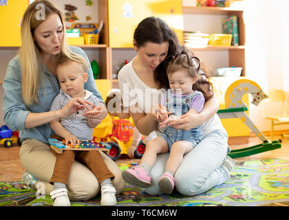 Bambini I bambini giocando con colorati giocattoli educativi insieme con le madri in vivaio per bambini Sala giochi Foto Stock