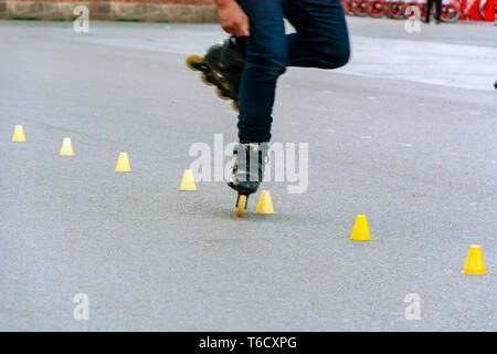 I piedi di un pattinatore mentre si esegue lo slalom tra il giallo dei coni di plastica posto in linea su asfalto Foto Stock