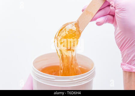 Concetto di zuccheraggio. vista della ciotola con la cosmetologia miele. bastone di legno Foto Stock