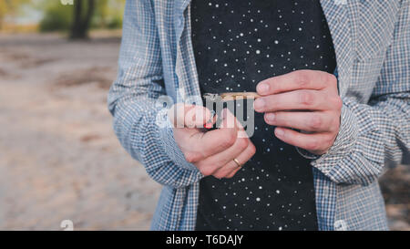 La persona fumare marijuana giunto all'esterno. Giunto di cannabis in mano Foto Stock