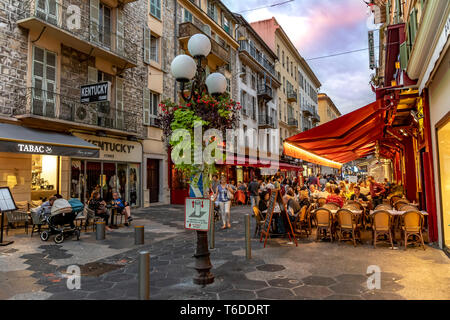 Nizza, Francia - 5 Ottobre 2018: Sera colpo di negozi e un ristorante con tavoli e sedie e persone sul marciapiede di una strada di Nizza, Francia. Foto Stock