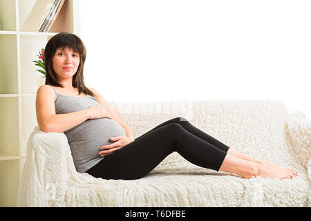 Donna incinta in appoggio sul divano Foto Stock