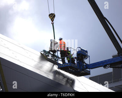 Due operai della costruzione su una piattaforma prendendo un pannello da una gru Foto Stock