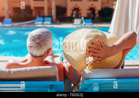 Famiglia Senior giovane a rilassarci in piscina giacente sulla chaise-longue. Le persone che si godono le vacanze estive. Foto Stock