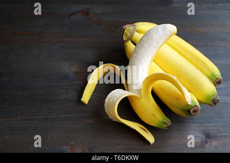 Una banana pelata su un grappolo di banane isolato in legno marrone scuro e tavolo con spazio di copia Foto Stock