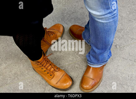 Due coppie di piedi con luce marrone stivali in pelle su sfondo grigio Foto Stock