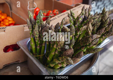 Un sacco di appena raccolto di punte di asparagi seduti in un metallo chef gastro tin con pomodori freschi nelle caselle dietro Foto Stock