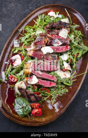 Italiano tradizionale di Tagliata di Manzo con parmigiano e insalata come close-up su una piastra Foto Stock