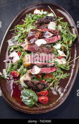 Italiano tradizionale di Tagliata di Manzo con parmigiano e insalata come close-up su una piastra Foto Stock