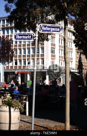 Worm, Germania - 13 Ottobre 2018: Un ben visitato cafe sul mercato superiore alle spalle di segnaletica stradale e di fronte al Skulptur Schicksalsrad il 1 ottobre Foto Stock