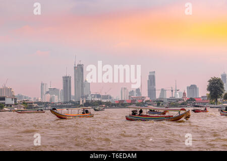 Barche sul Fiume Chao Phraya con edifici in background in Bangkok, capitale della Thailandia nel sud-est asiatico al tramonto Foto Stock