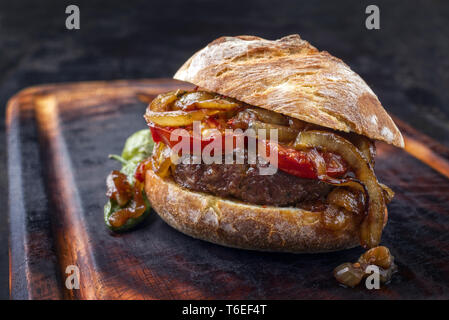 Barbecue Wagyu Hamburger con cipolle e pomodori come close-up su un olocausto tagliere Foto Stock