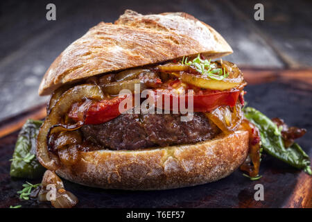 Barbecue Wagyu Hamburger con cipolle e pomodori come close-up su un olocausto tagliere Foto Stock