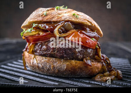 Barbecue Wagyu cheeseburger con cipolle e pomodori come close-up su un grillage Foto Stock